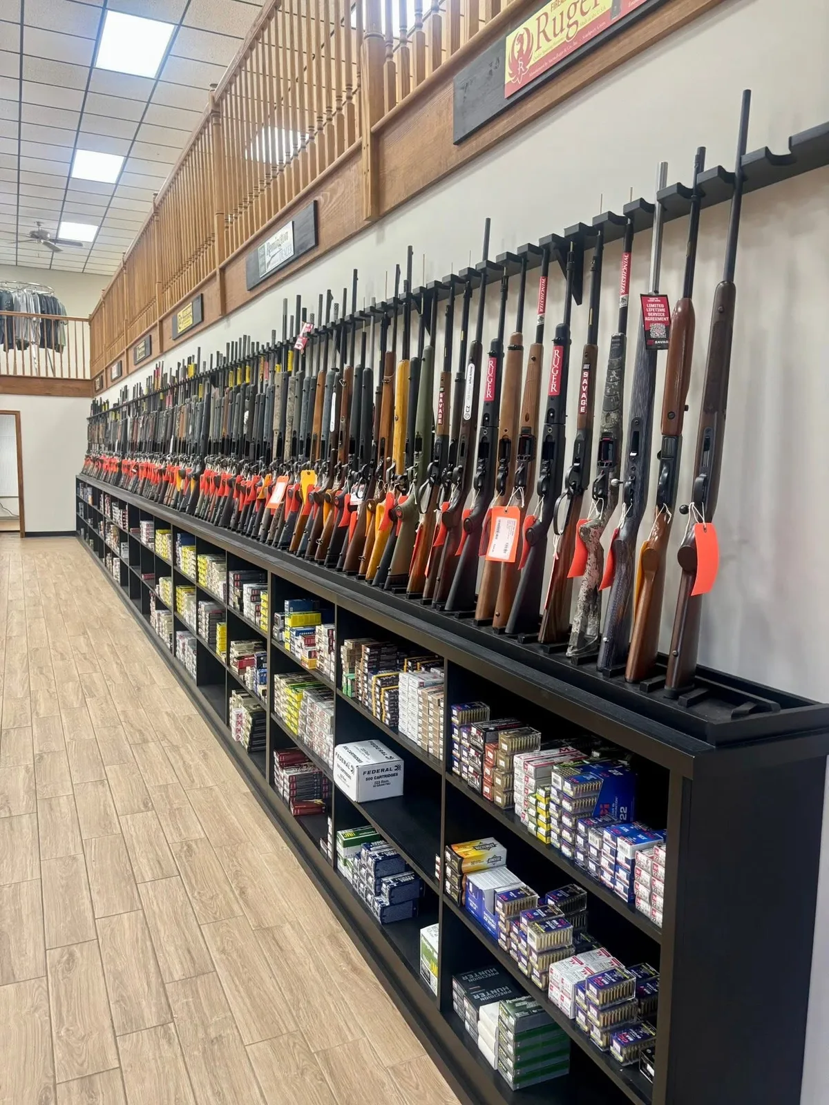 A long wall rack of rifles and shotguns above shelves stocked with ammunition
