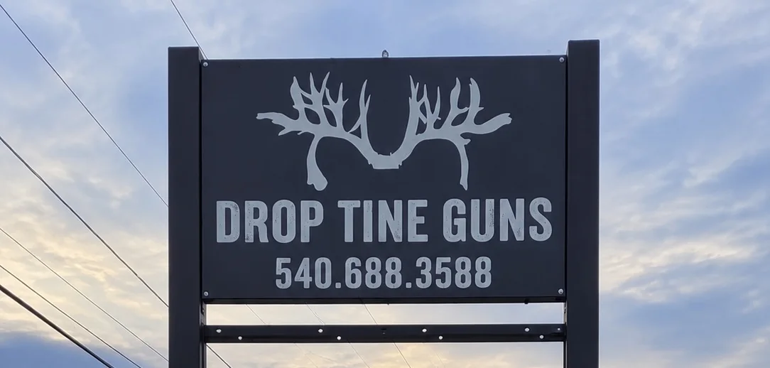 The Drop Tine Guns sign at the road, showing the antler logo and the shop phone number