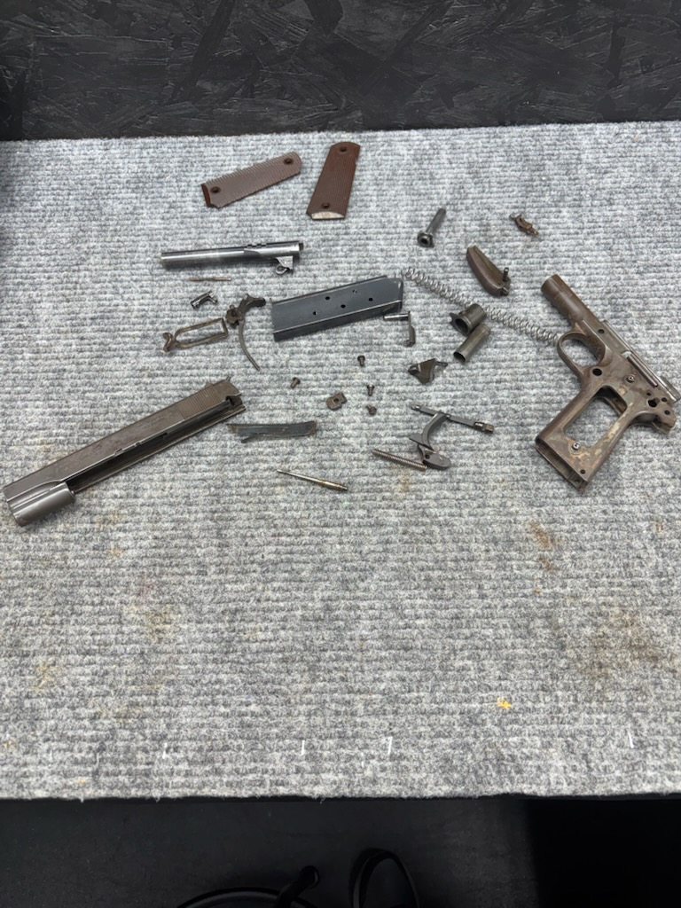 1943 U.S. Army issue 1911 pistol from World War II before restoration, disassembled with a rusted frame, at Drop Tine Guns in Staunton, VA